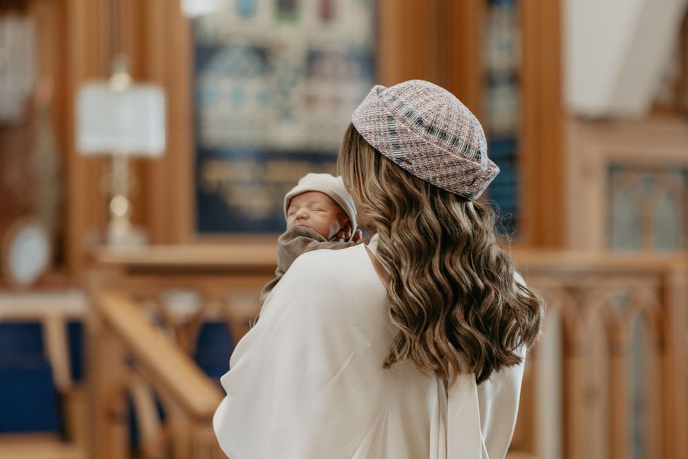 A person wearing a knitted beanie and white sweater stands in a church with long wavy brown hair.