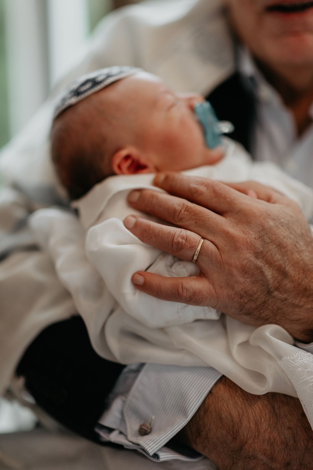 Close-up view of hands holding a baby wearing a kippah during a Jewish religious ceremony.