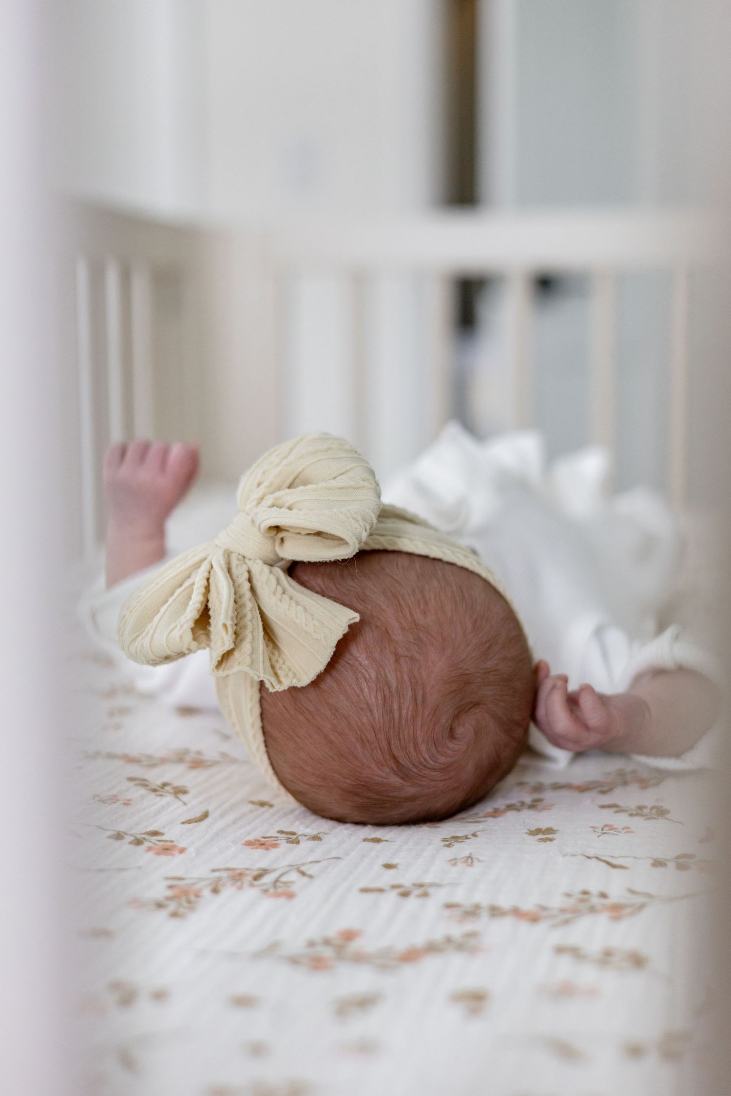 A newborn baby's head rests on a floral patterned blanket with a white bow.