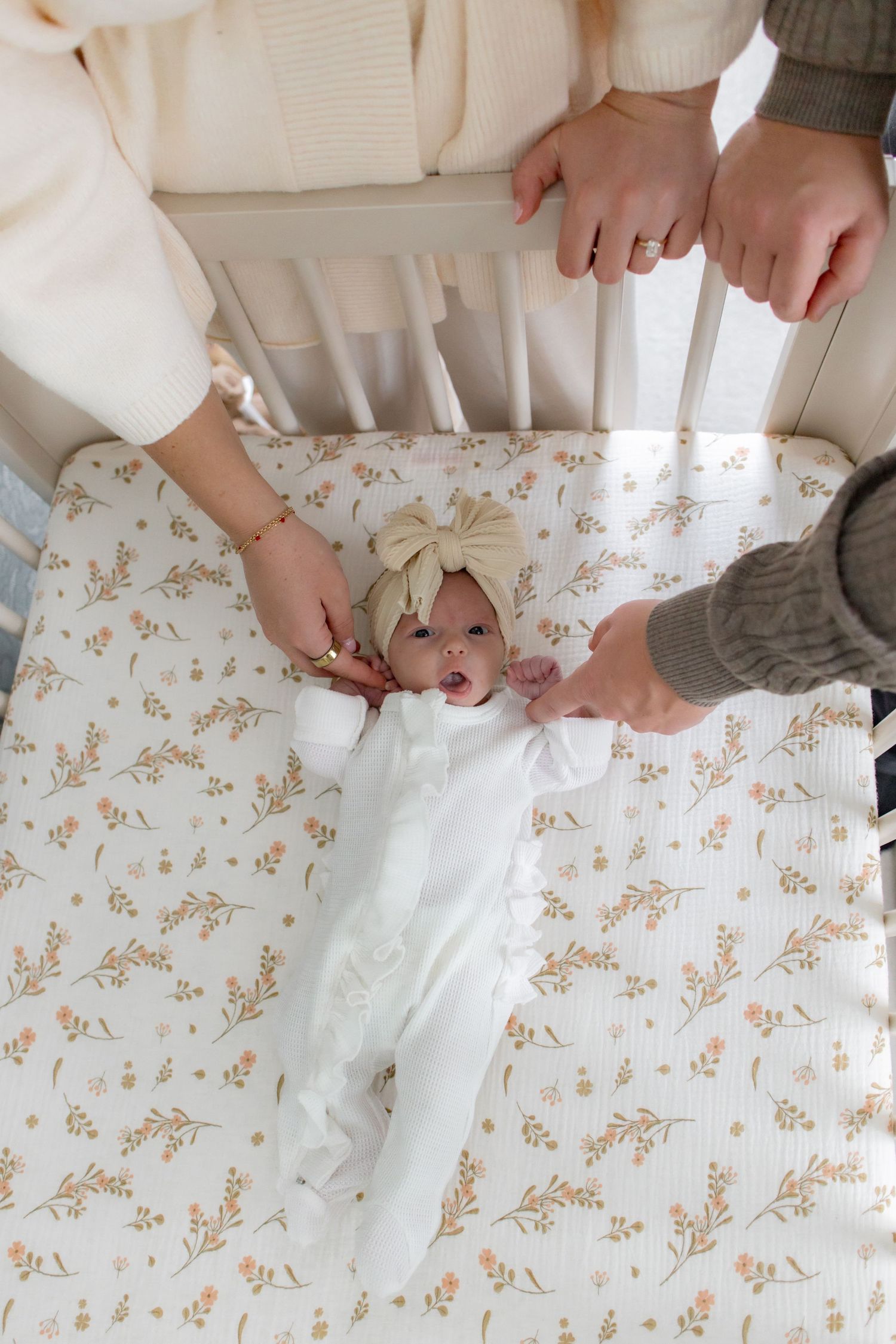 Hands fold a white fitted sheet on a floral patterned surface in a step-by-step sequence.