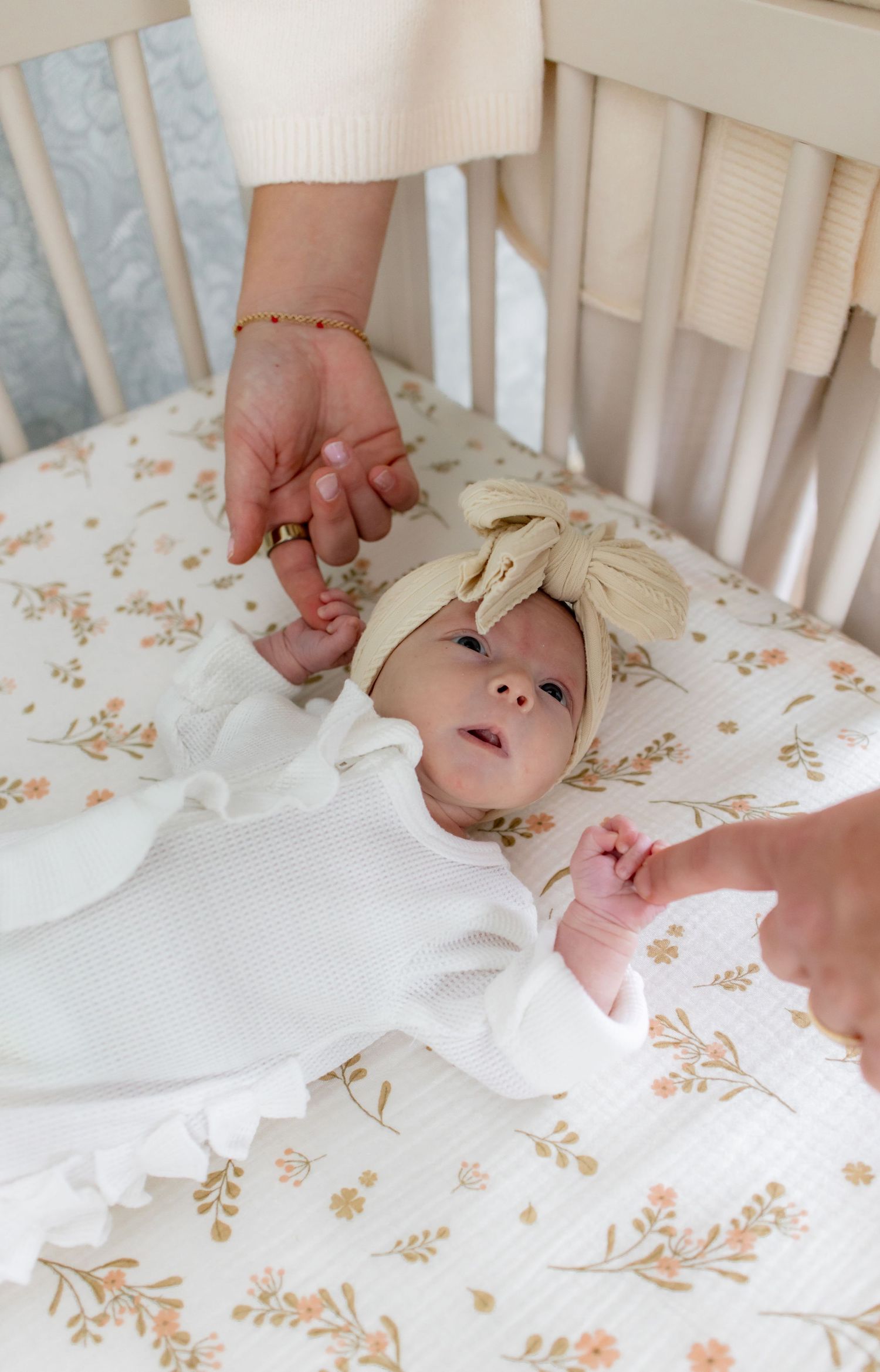 Newborn baby lying on floral crib sheets while being gently touched by caring hands.