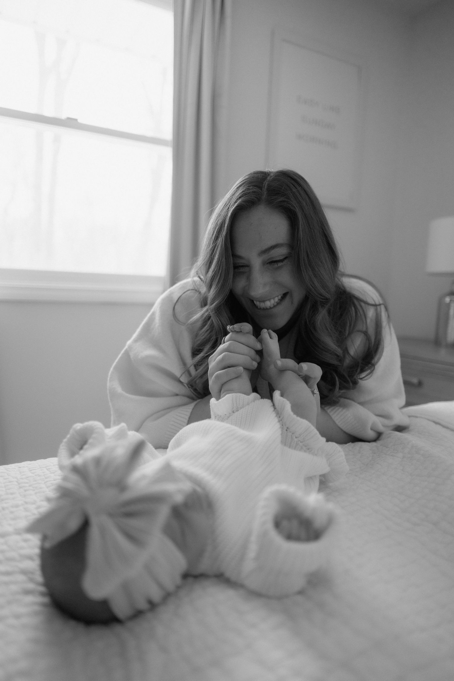 Black and white photo series showing a tender moment between parent and newborn on white bedding.