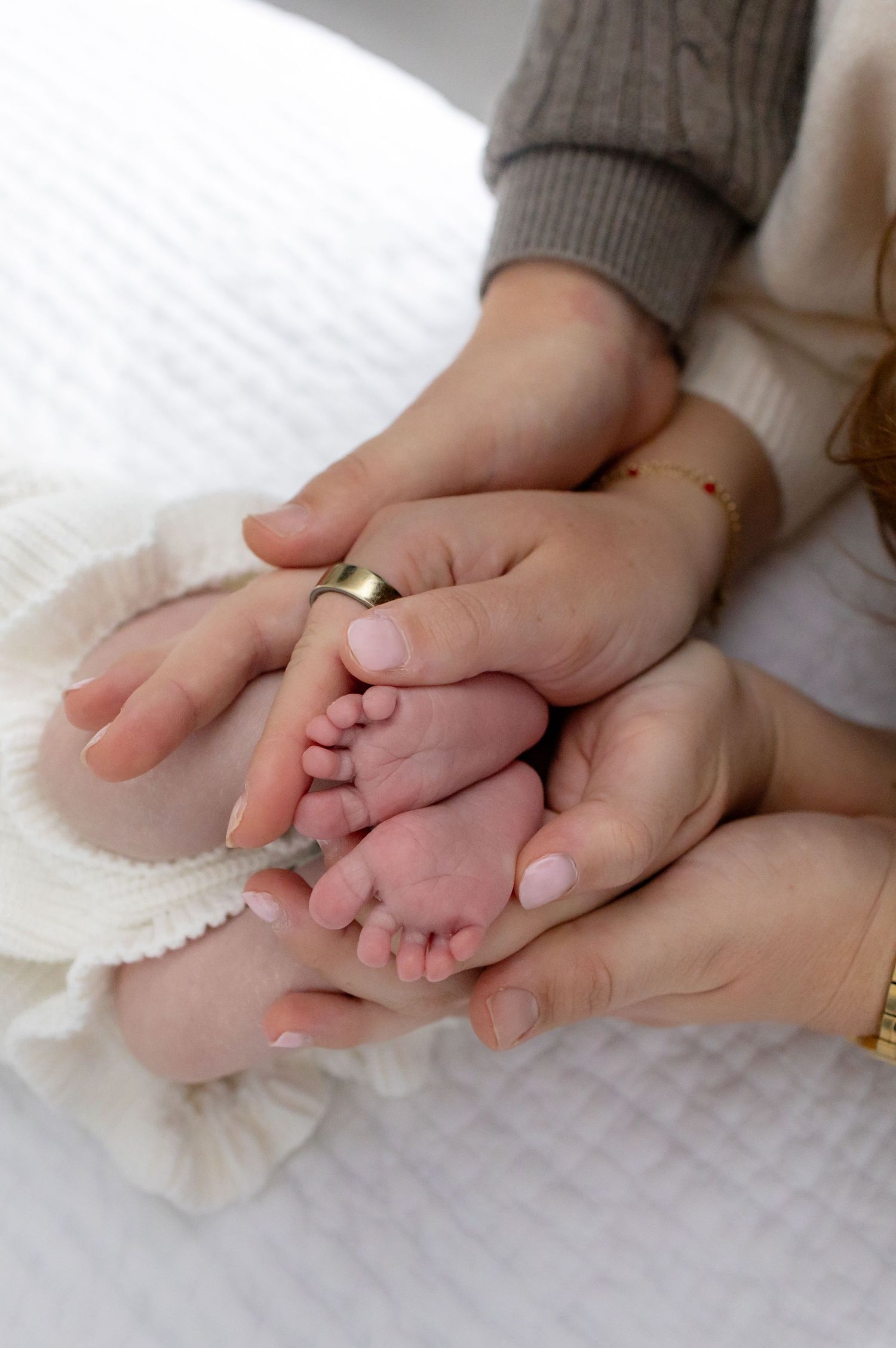 Adult hands gently cradle a newborn baby's tiny feet on soft white fabric.