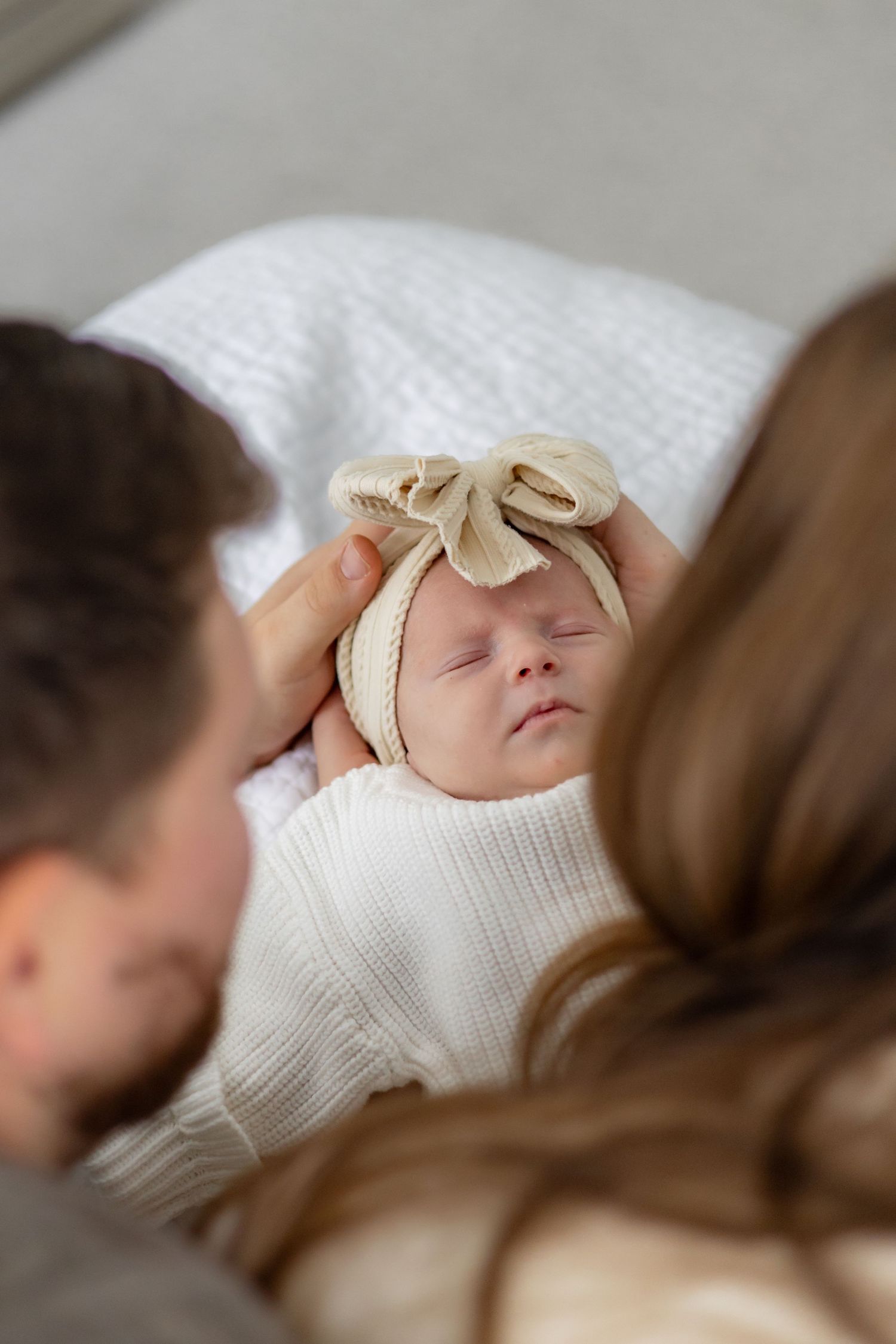 A sleeping baby wearing a white knit sweater and cream bow headband.