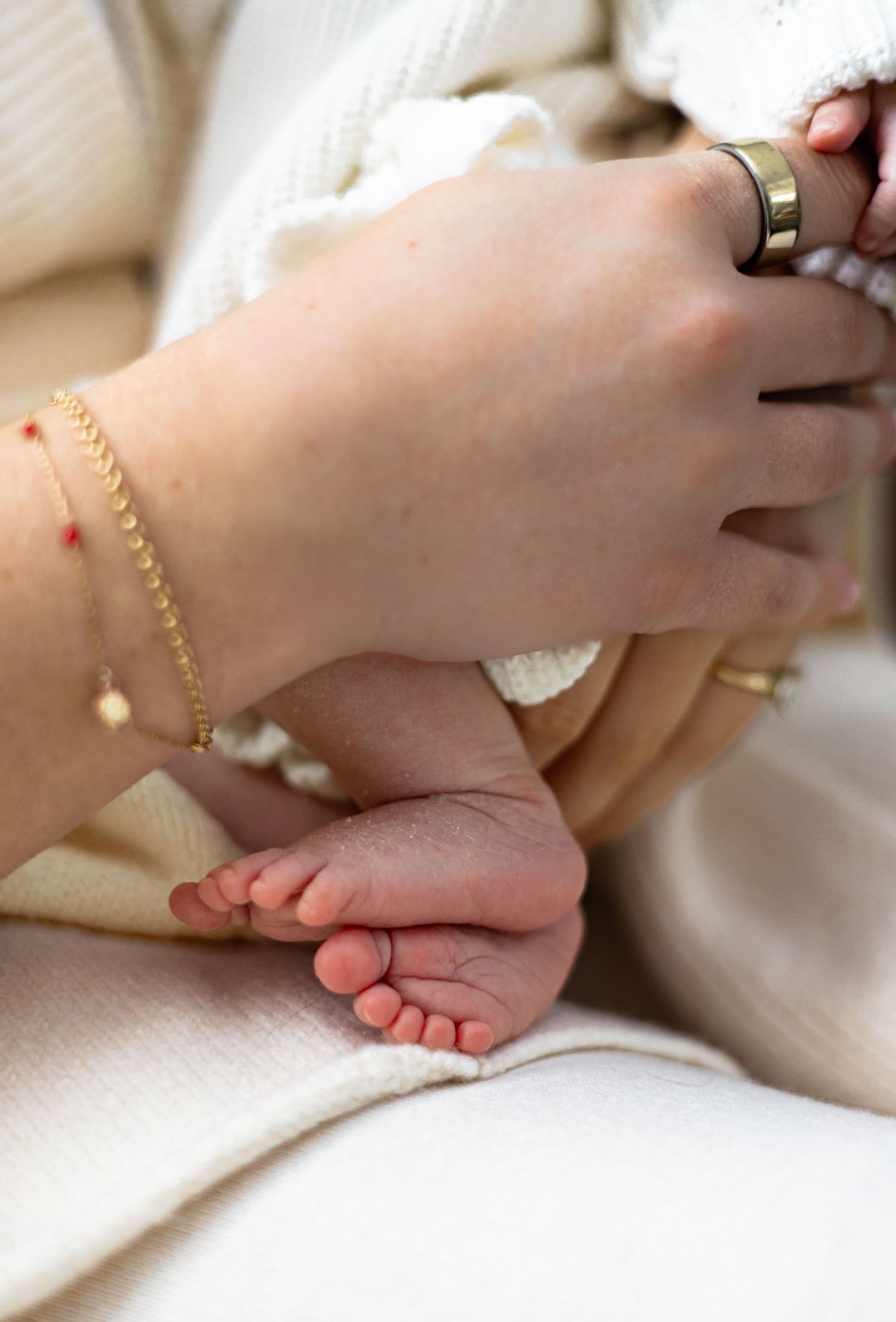 Close up of delicate gold bracelet and tiny baby feet on soft cream fabric.