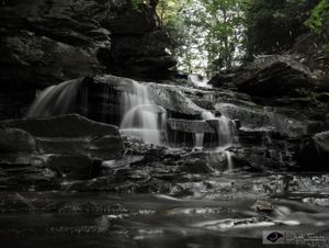 Garden Creek Falls cascades over rugged black rocks, framed by lush green trees. Captured by Jeff Fevens Photography in Fredericton NB.