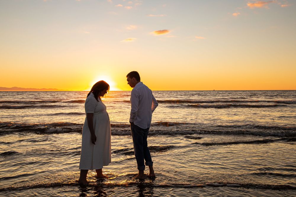 Silhouettes of two people walking along a beach at sunset with orange sky and rolling waves.