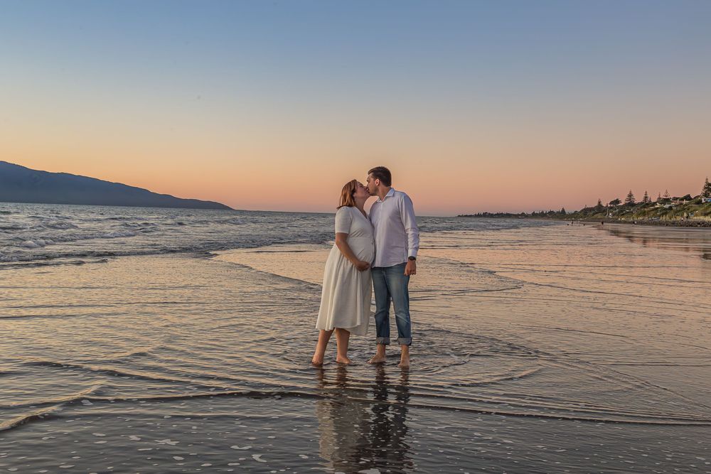 Couple walking together on a tranquil beach at sunset with gentle waves lapping at the shore.