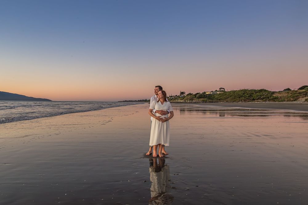 Scenic beach landscape at sunset with soft pink and orange sky reflecting on calm ocean waters.