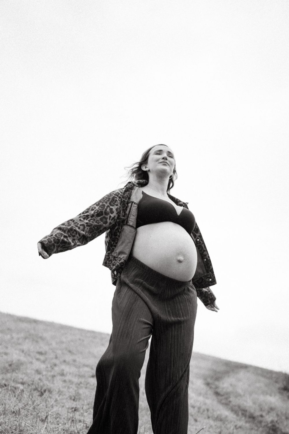 Expectant mother wearing black outfit poses confidently against overcast sky.