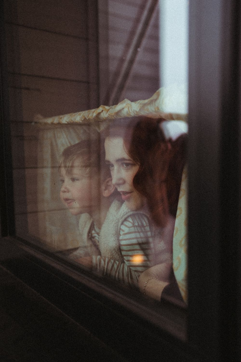 Artistic portrait through window reflection showing figures gazing outward in dreamy lighting.