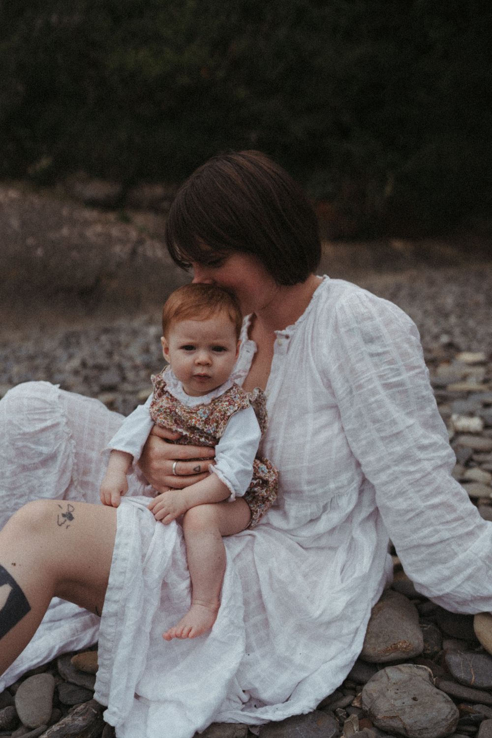 Natural portrait showing tender moment between parent and baby sitting on rocky shore.
