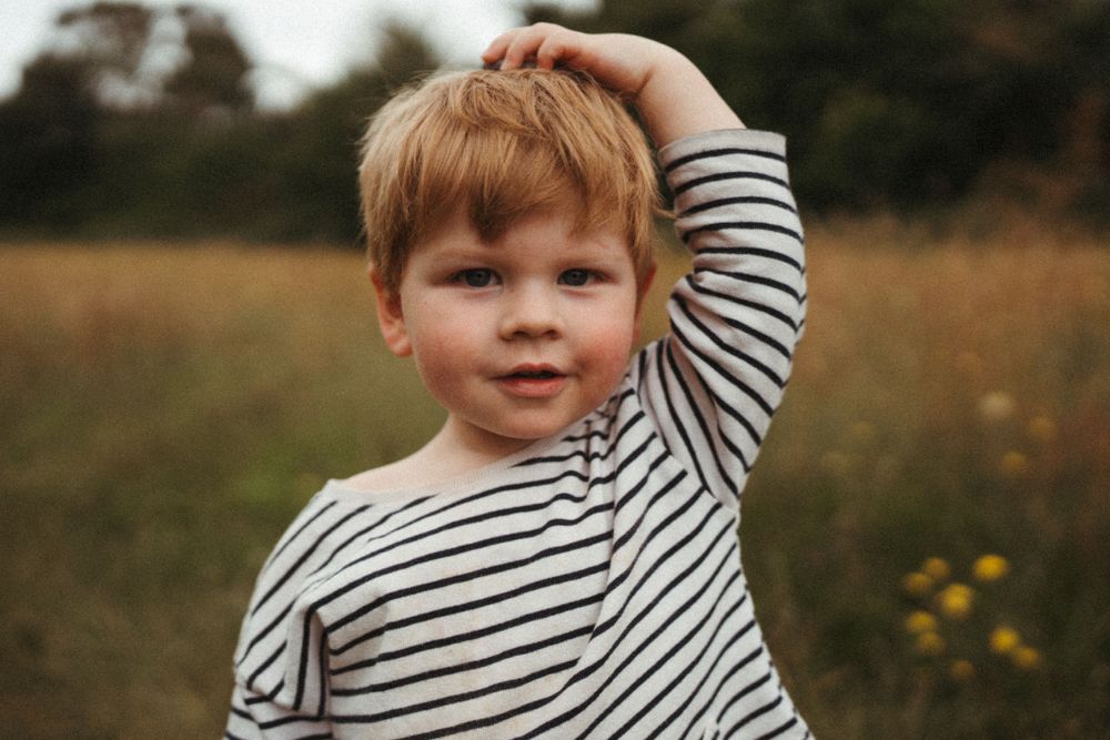 Child in striped shirt plays in a field of tall grass at golden hour.