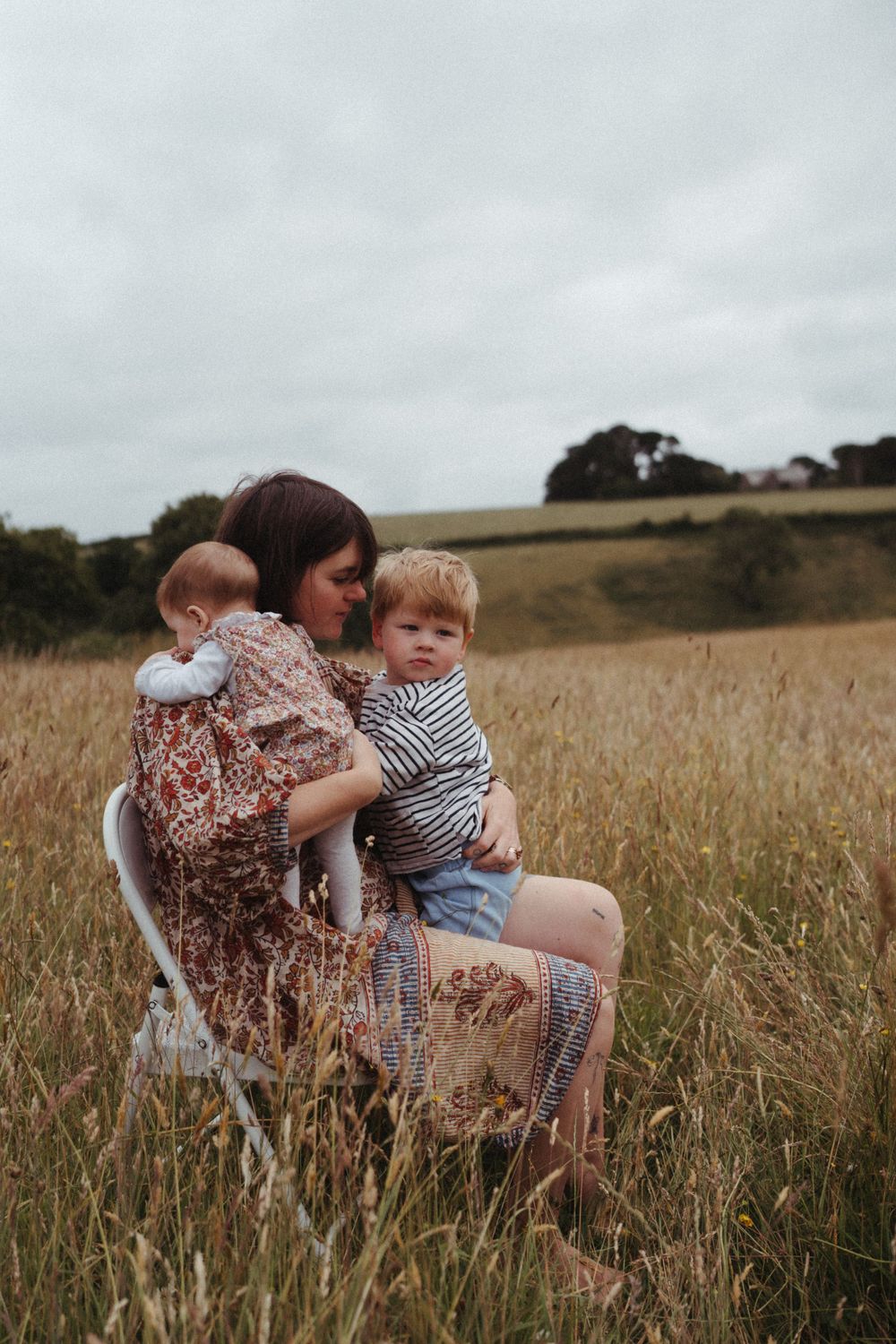 A tender family moment captured in a golden field with tall grass and cloudy skies.