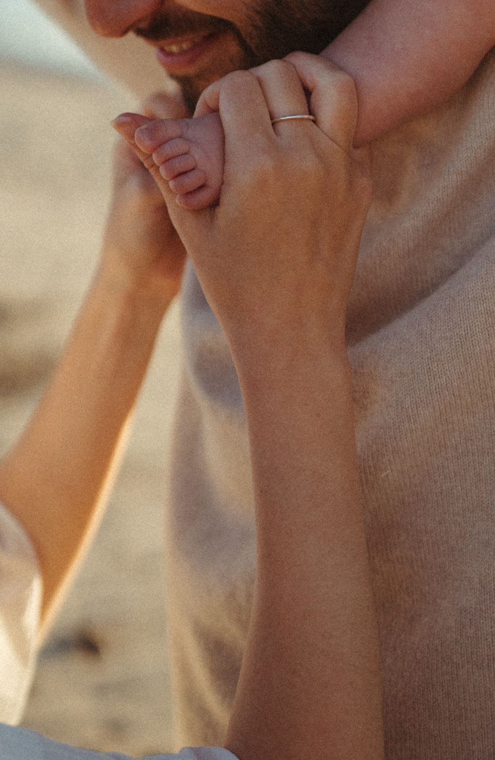 Close-up of hands holding tiny baby feet with wedding ring visible.