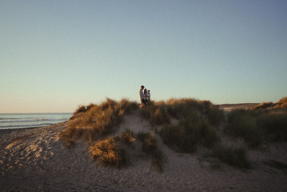 Silhouetted figures standing on coastal sand dunes at dusk.
