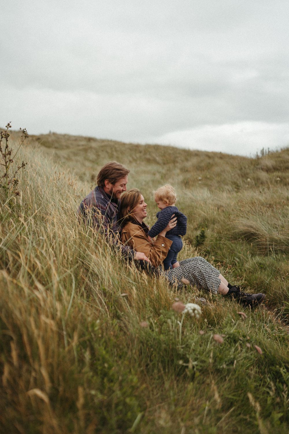 Family relaxing together on a grassy hillside overlooking a coastal landscape.