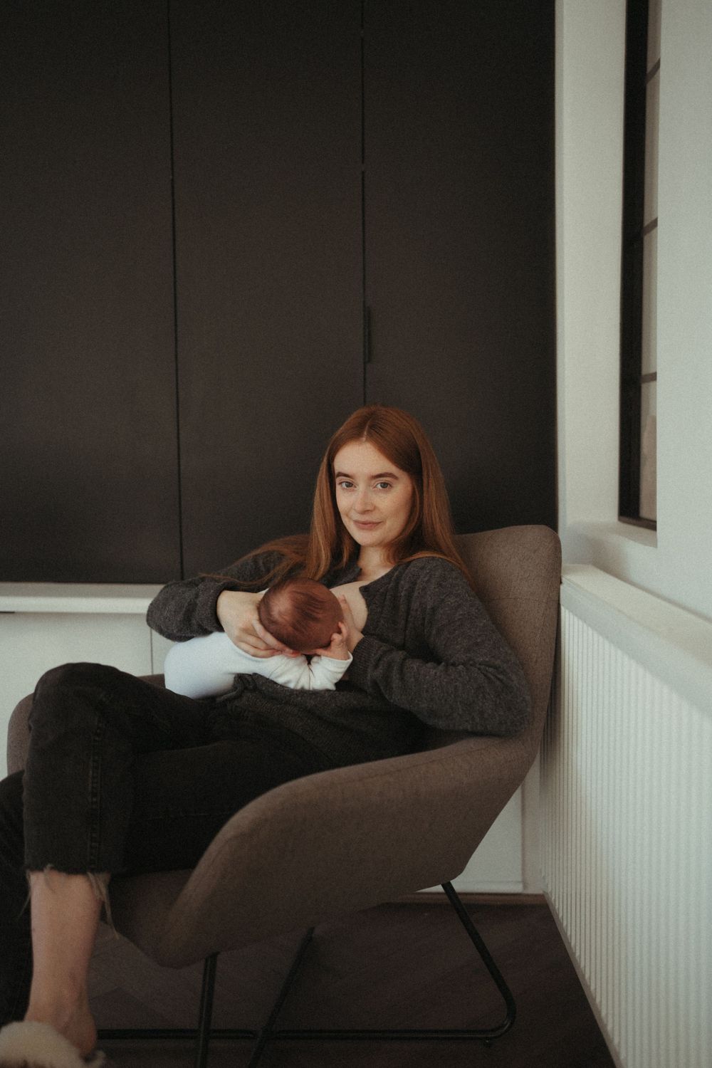 Person relaxing in modern gray armchair while holding infant.