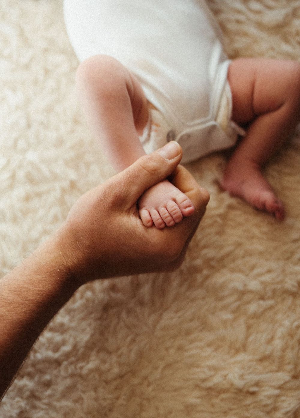 Close-up of adult hand gently holding tiny baby feet on plush carpet.