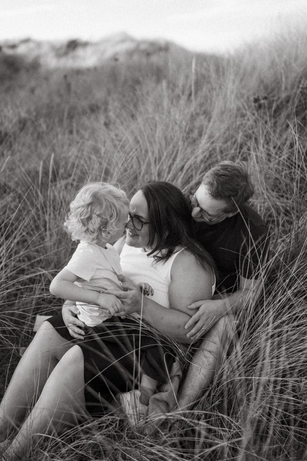 Family enjoying tender moment together in tall beach grass.