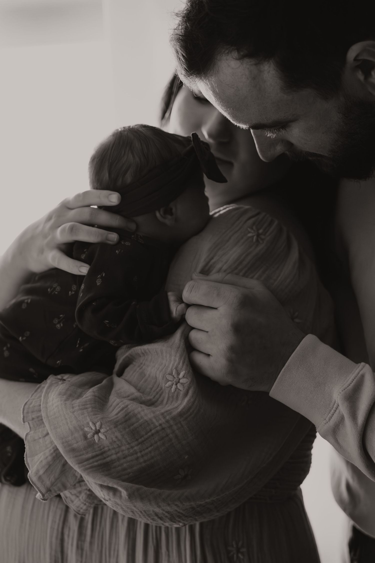 A tender black and white photo sequence showing someone gently kissing a baby's forehead in four progressive frames.