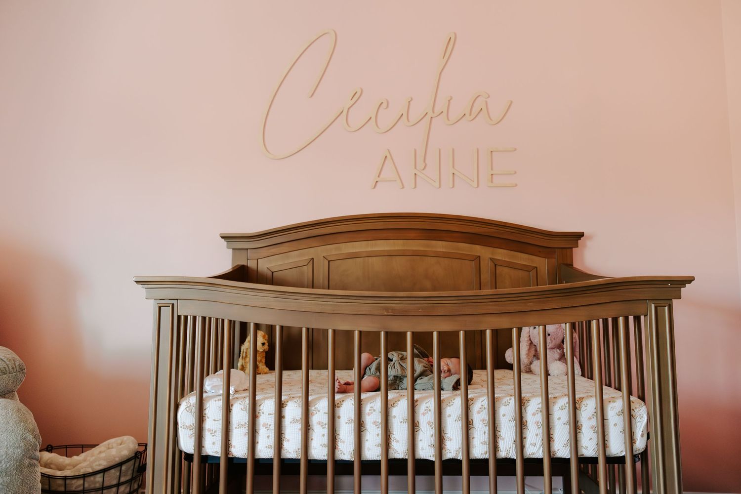 A wooden baby crib with cursive text on the wall above it in a nursery with pink walls.