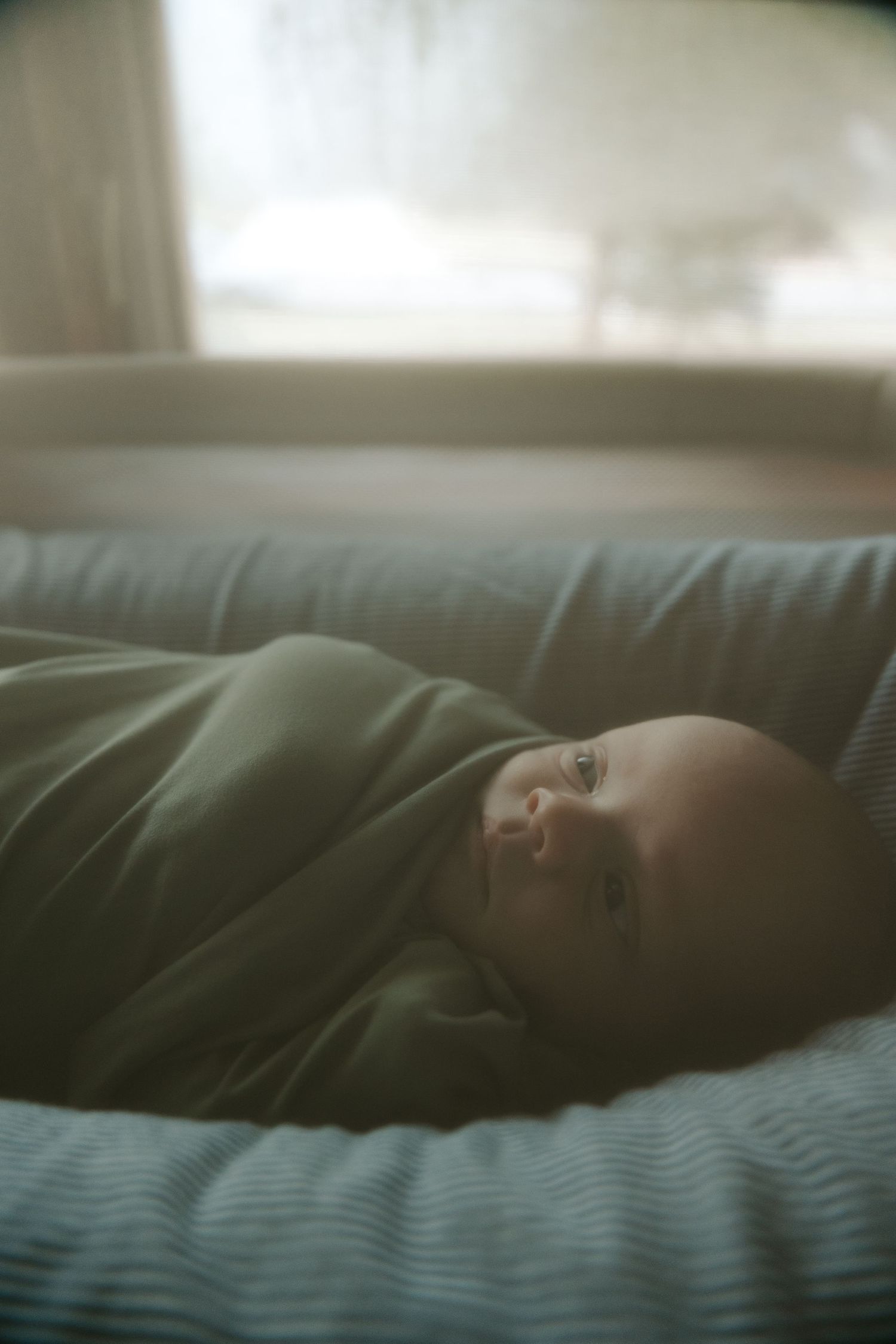 Person resting on dark couch in soft natural window light creating moody atmospheric scene.