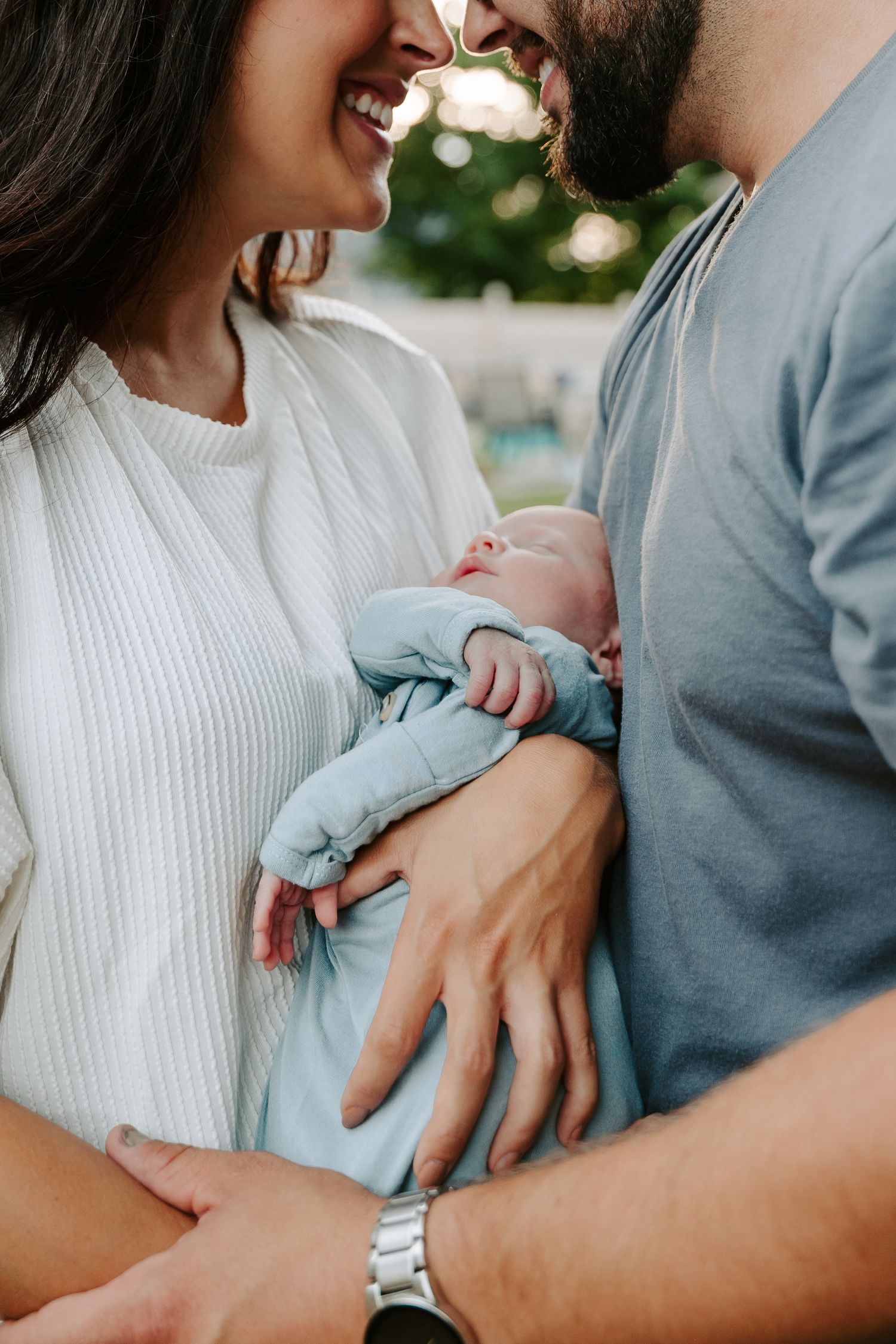 A couple in white and grey clothing share tender moments while holding their newborn baby in a series of intimate photos.