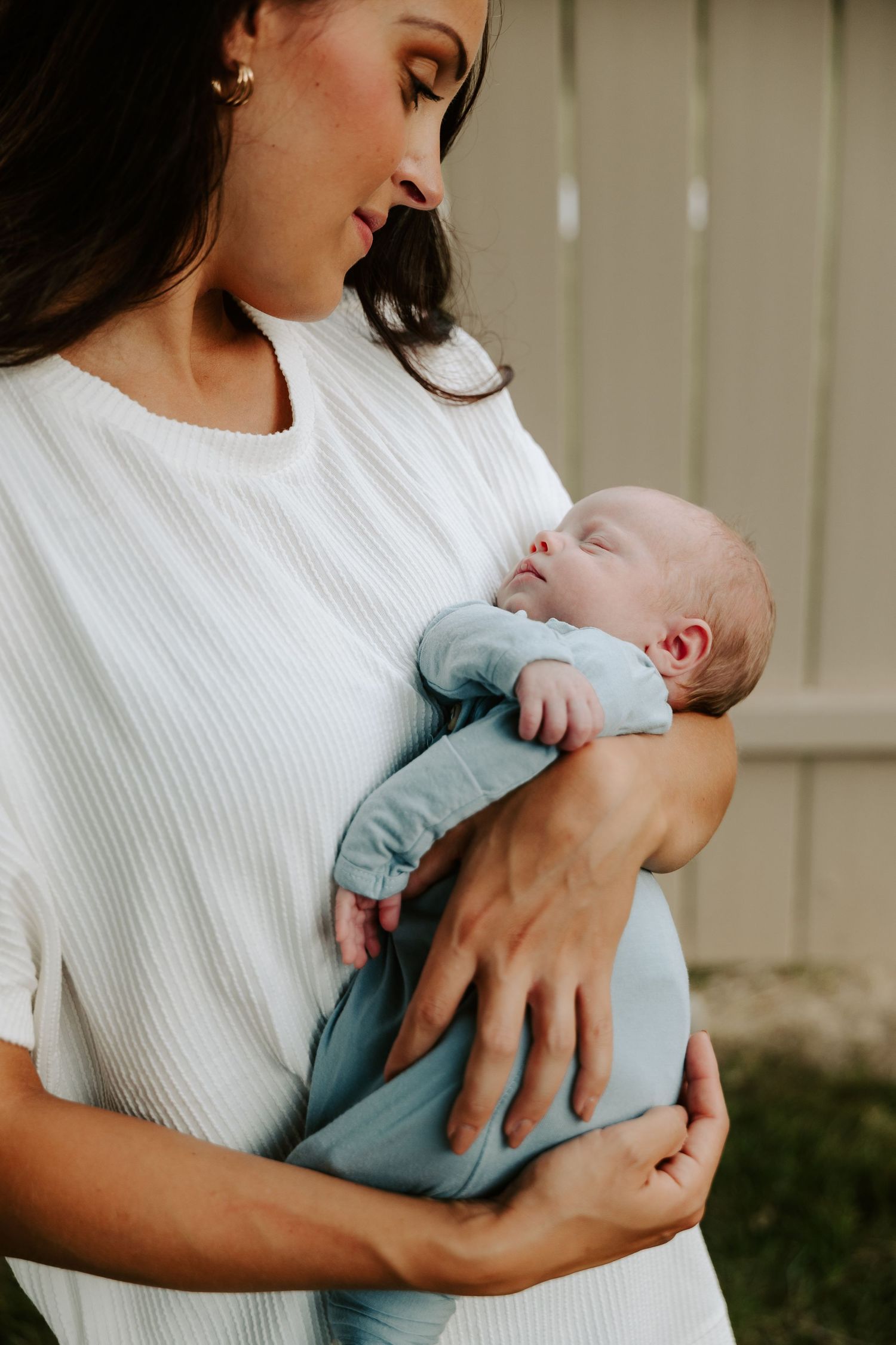 A tender moment captured as a mother in a white sweater cradles her sleeping newborn baby wearing light blue.