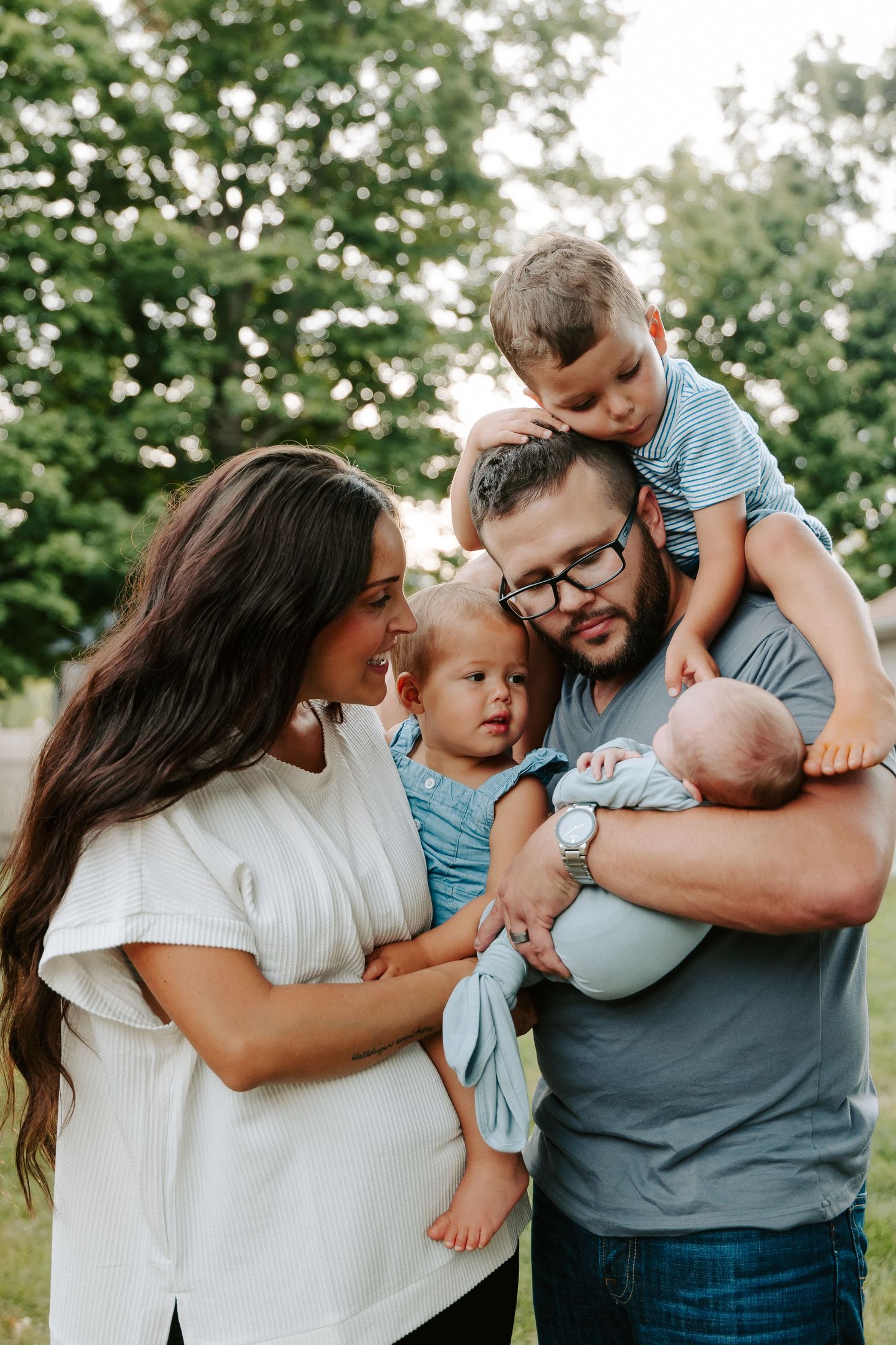 A loving family shares tender moments together in a series of outdoor portraits against a green leafy background.