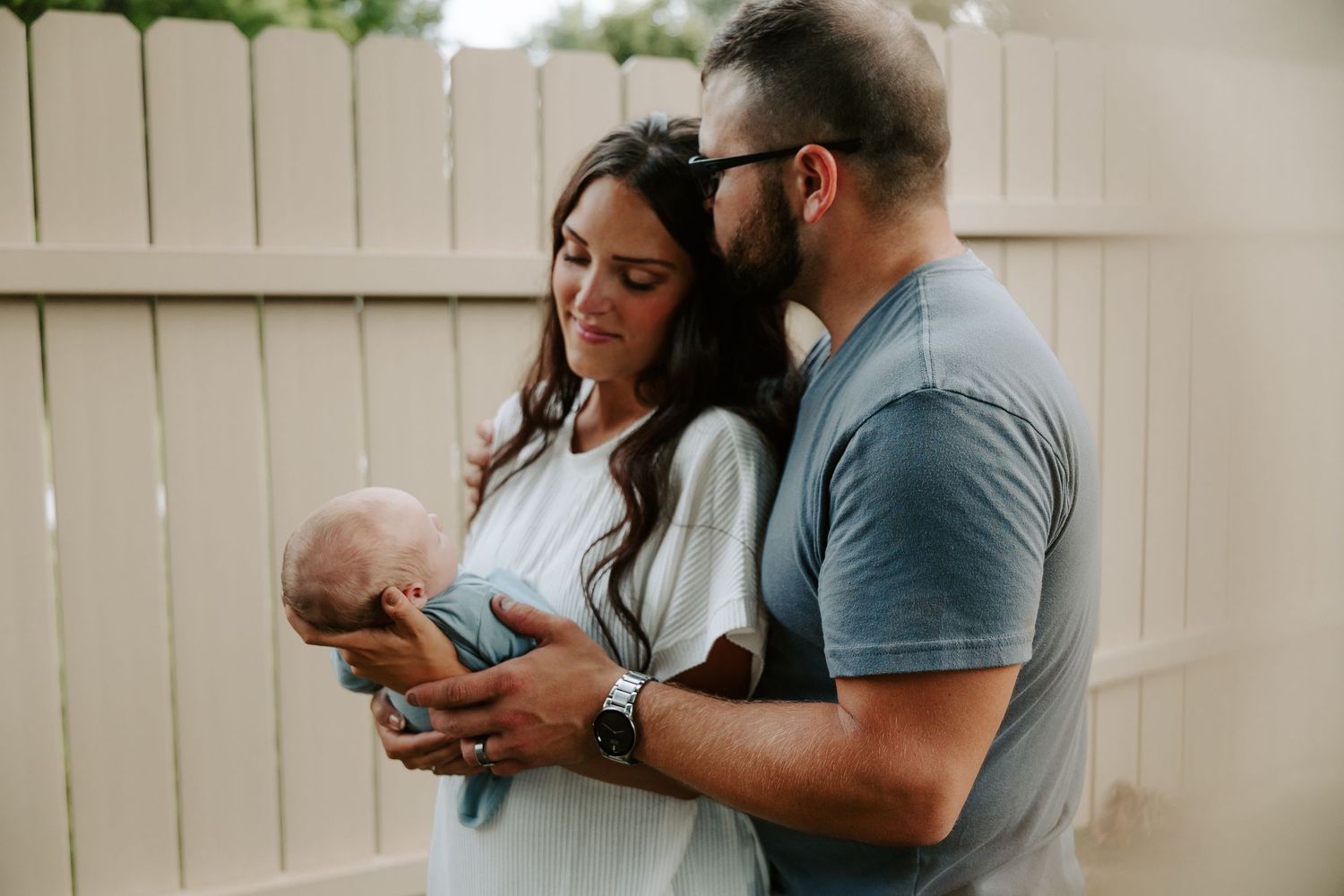 A couple in casual attire holds and gazes lovingly at their newborn baby in a cozy indoor setting.