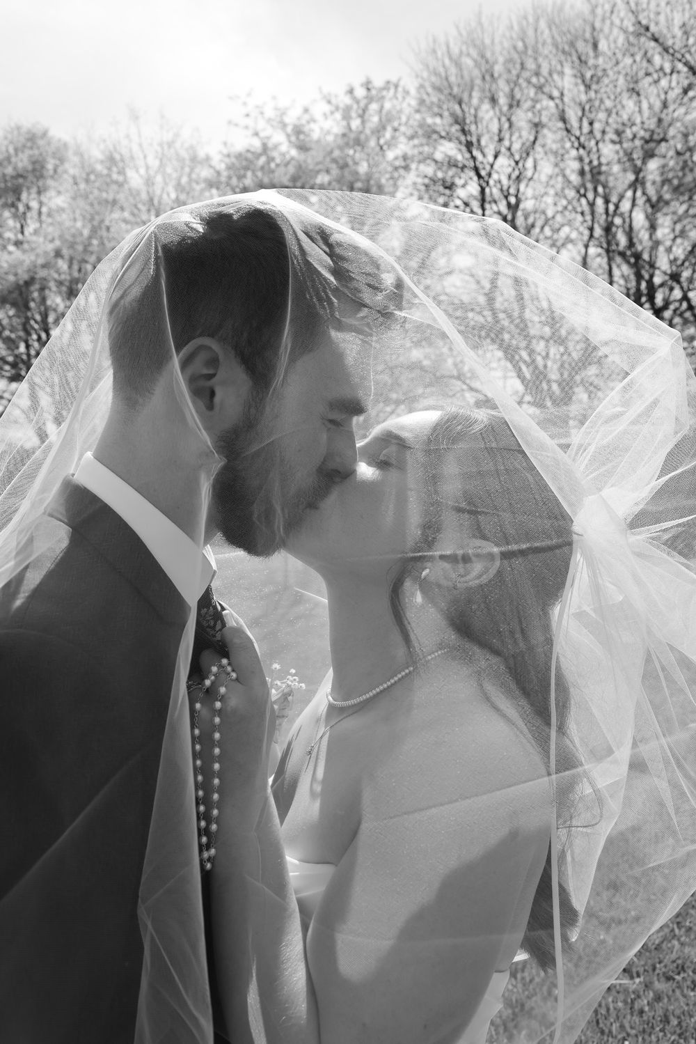 Romantic black and white wedding photo with couple kissing under flowing veil.
