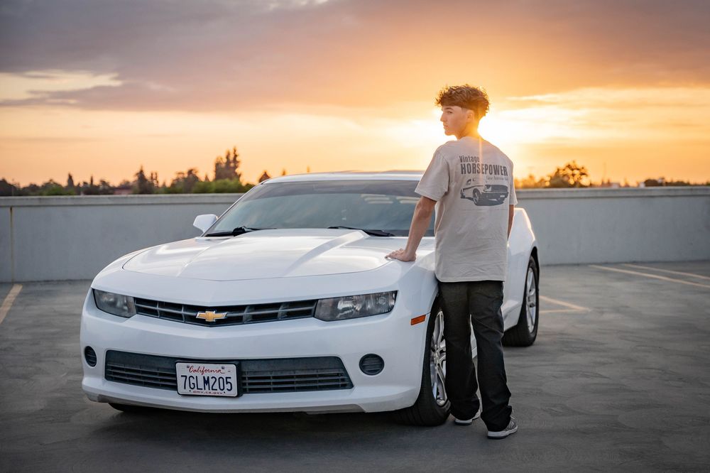 A white Chevrolet Camaro sports car parked at sunset on an empty lot with dramatic orange sky in the background.