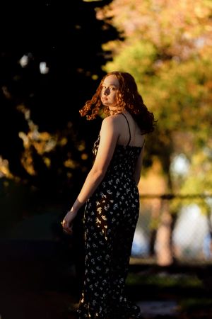 Woman in floral dress walking through autumn park during golden hour sunset.