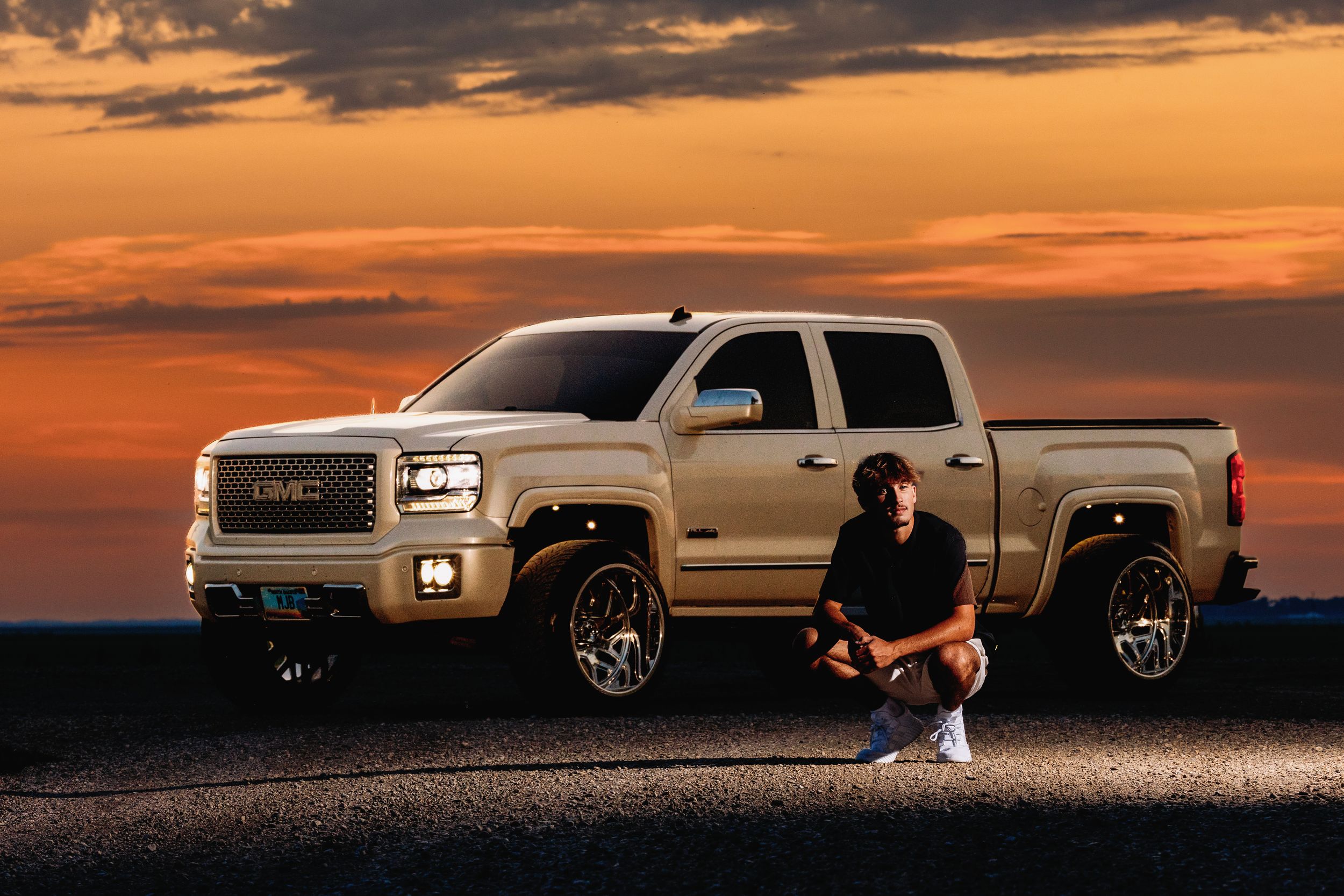 A silver pickup truck silhouetted against a dramatic orange sunset sky creates a striking panoramic view.