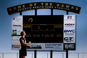 Baseball player crouching at home plate under Home of the Hawks scoreboard at sunset.