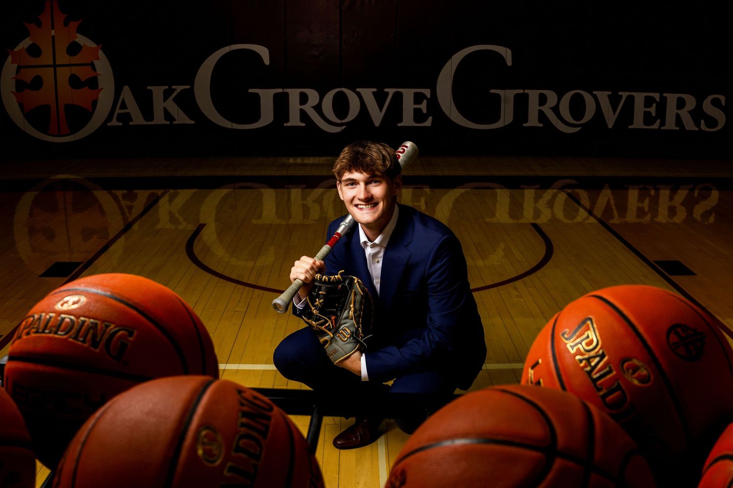 Young man poses with basketballs on a court in front of an Oak Grove Grovers banner.