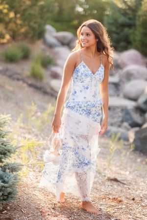 Someone poses in a delicate white and blue floral maxi dress on a rocky nature trail during golden hour.