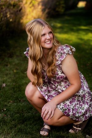 A person in a floral dress crouches in a grassy outdoor setting during a summer photoshoot.