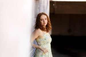 A woman in a floral dress poses near a window in soft natural light.