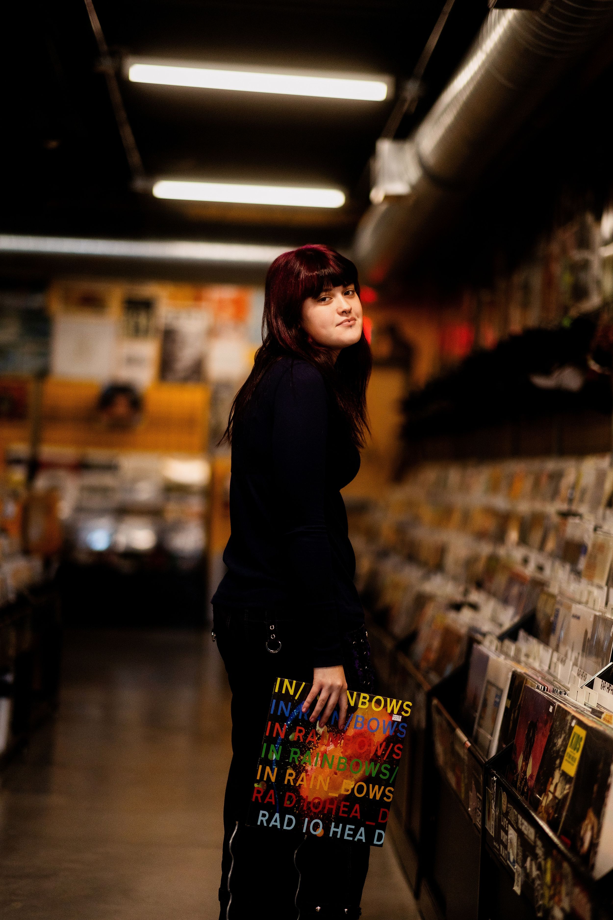 Person in black clothing browses vinyl records at a music store under fluorescent lighting.