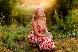 A person in a red and white floral dress sits in a sun-drenched meadow at golden hour.