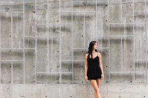 Minimalist fashion portrait against concrete wall in black dress.