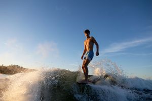 Silhouetted figure surfing on wave during sunset against blue sky.