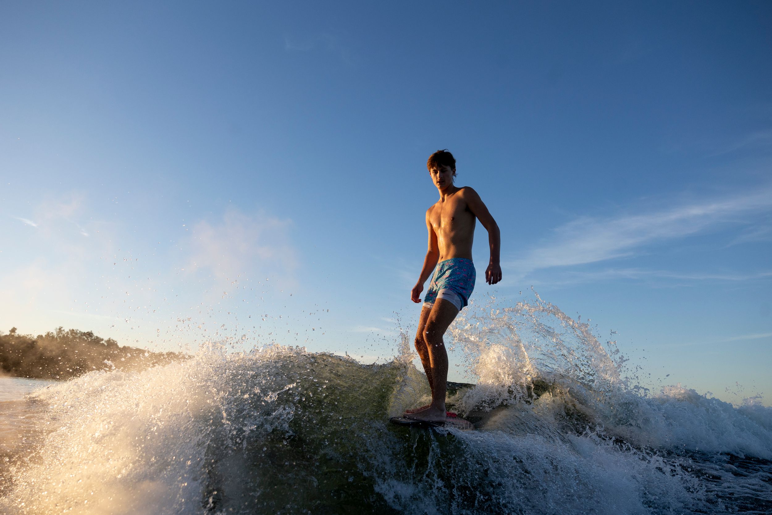 Silhouetted figure surfing on wave during sunset against blue sky.