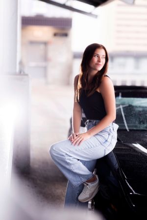Casual portrait against blurred garage background featuring denim jeans and dark top.