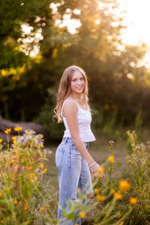 Golden hour senior portrait session in a wildflower field with light denim overalls.