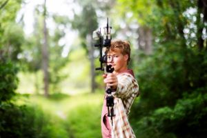 Archer in camouflage clothing aims bow in forest setting.