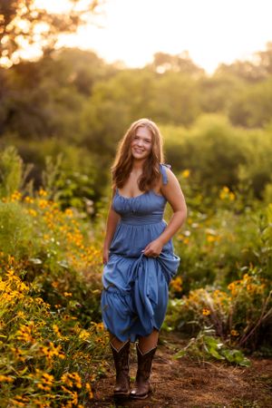 A flowing navy blue dress swirls among yellow wildflowers during golden hour.