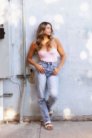 Casual summer fashion pose against white wall with pink top and light denim.